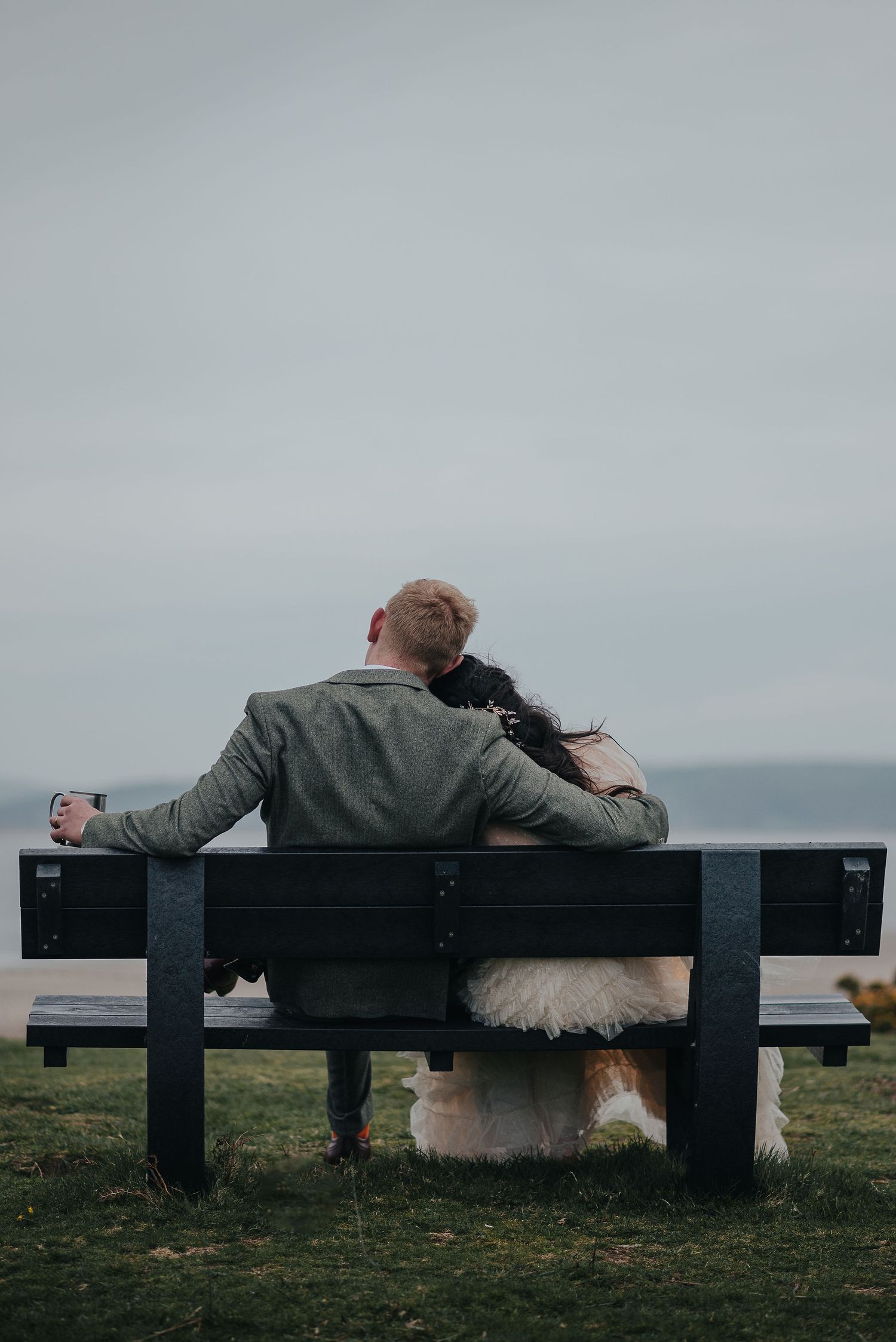 A romantic moment on a bench overlooking the ocean in wedding attire.