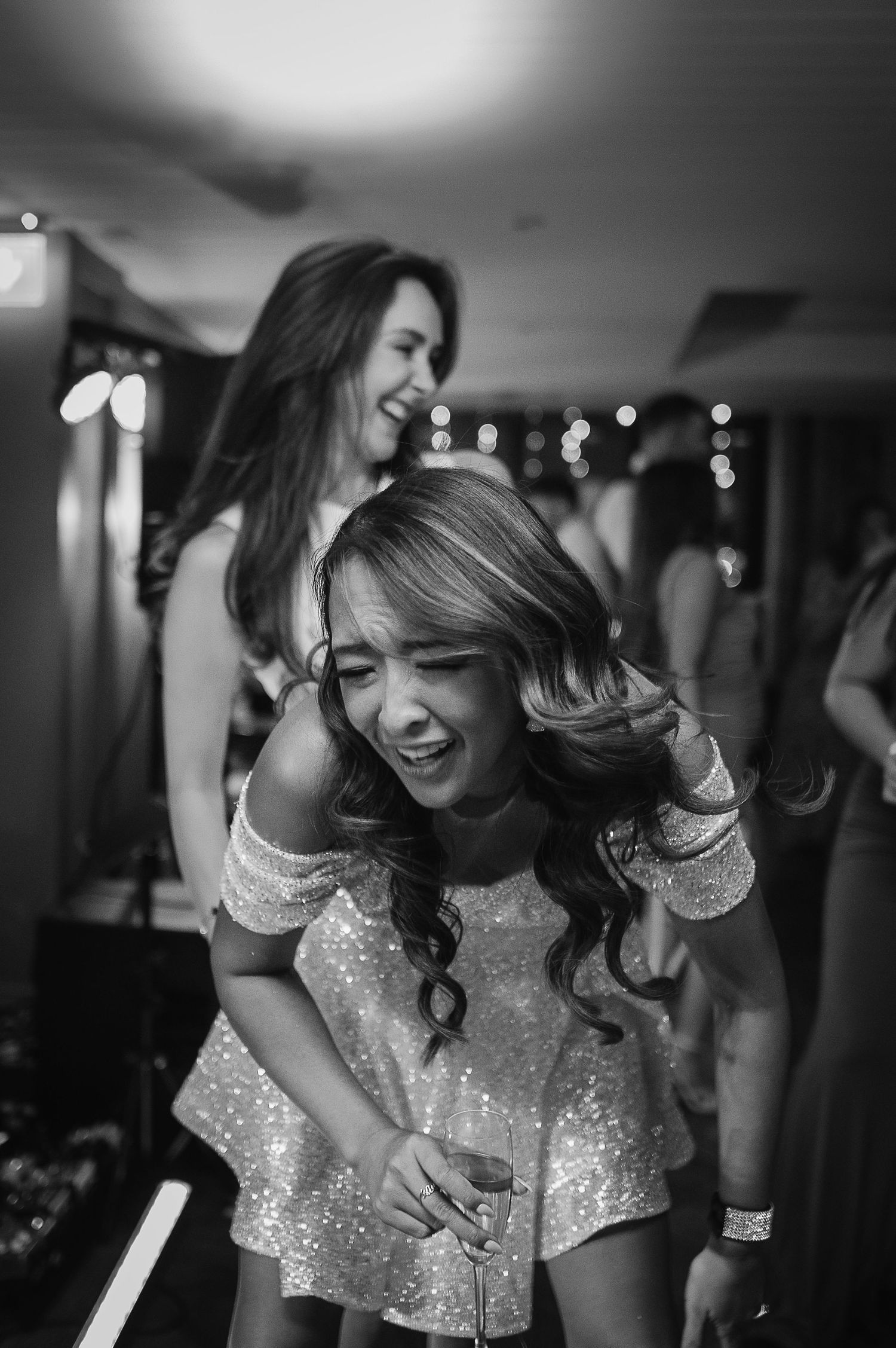 Two friends laughing and dancing together in sparkling dresses at a festive party.