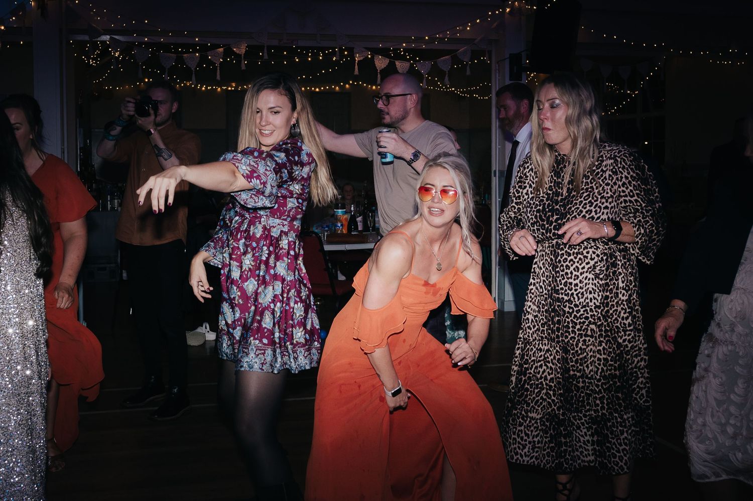 Party guests dance together under string lights in festive dresses.