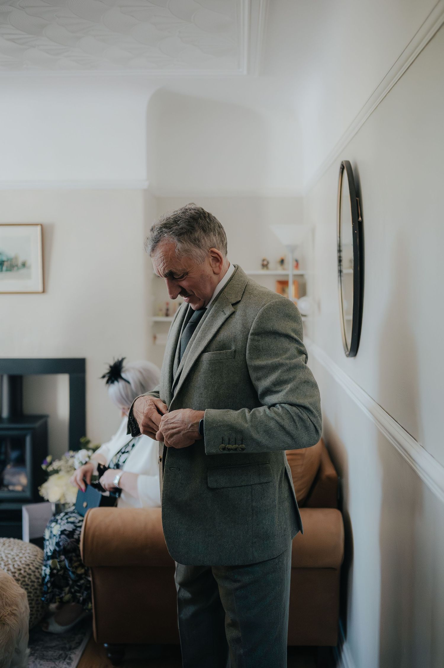 A person in a gray suit adjusting their tie in a living room setting.