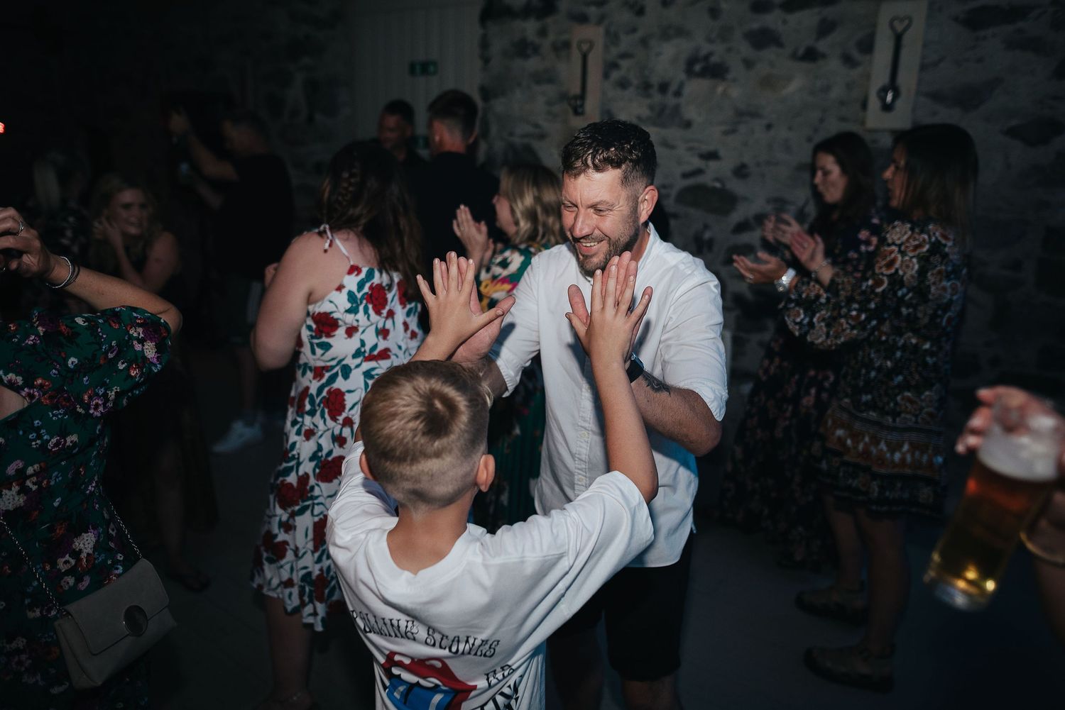 Wedding guests dancing and celebrating at a dimly lit reception venue.