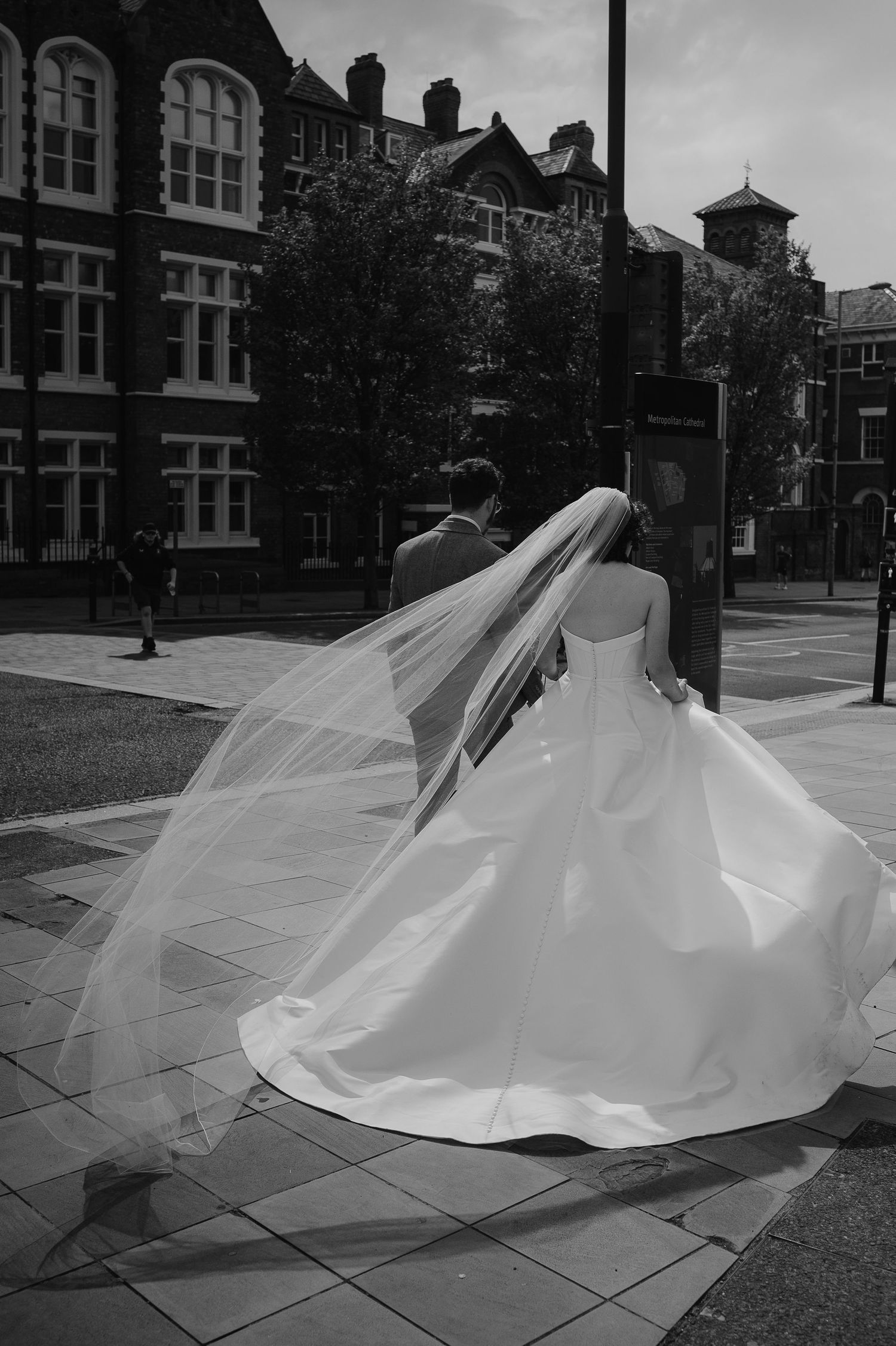 A wedding dress billows in the wind against historic architecture backdrop.