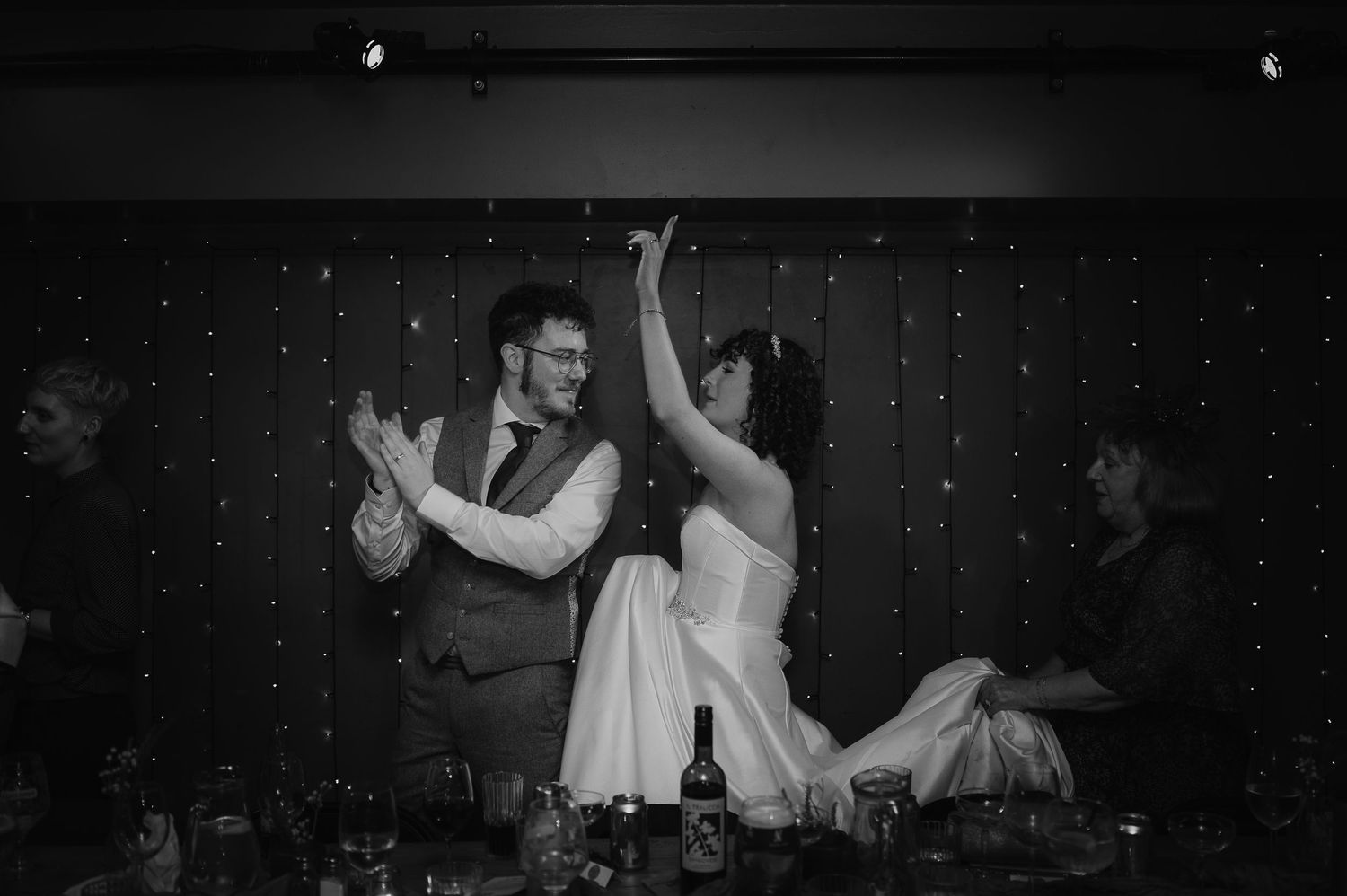 Couple dances energetically during wedding reception with sparkly backdrop.