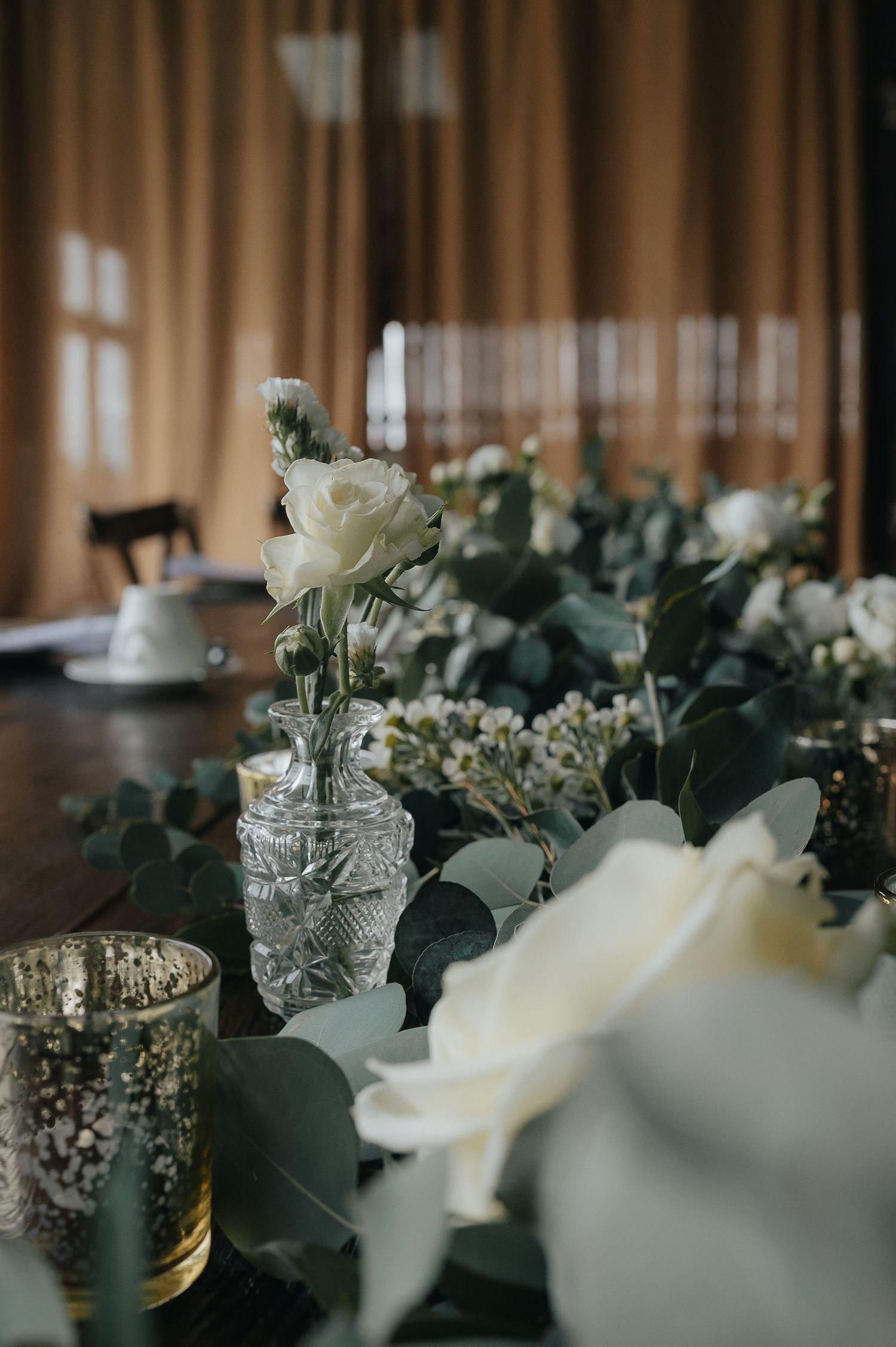 Elegant table setting with white roses and eucalyptus in crystal vases and gold mercury glass votives.