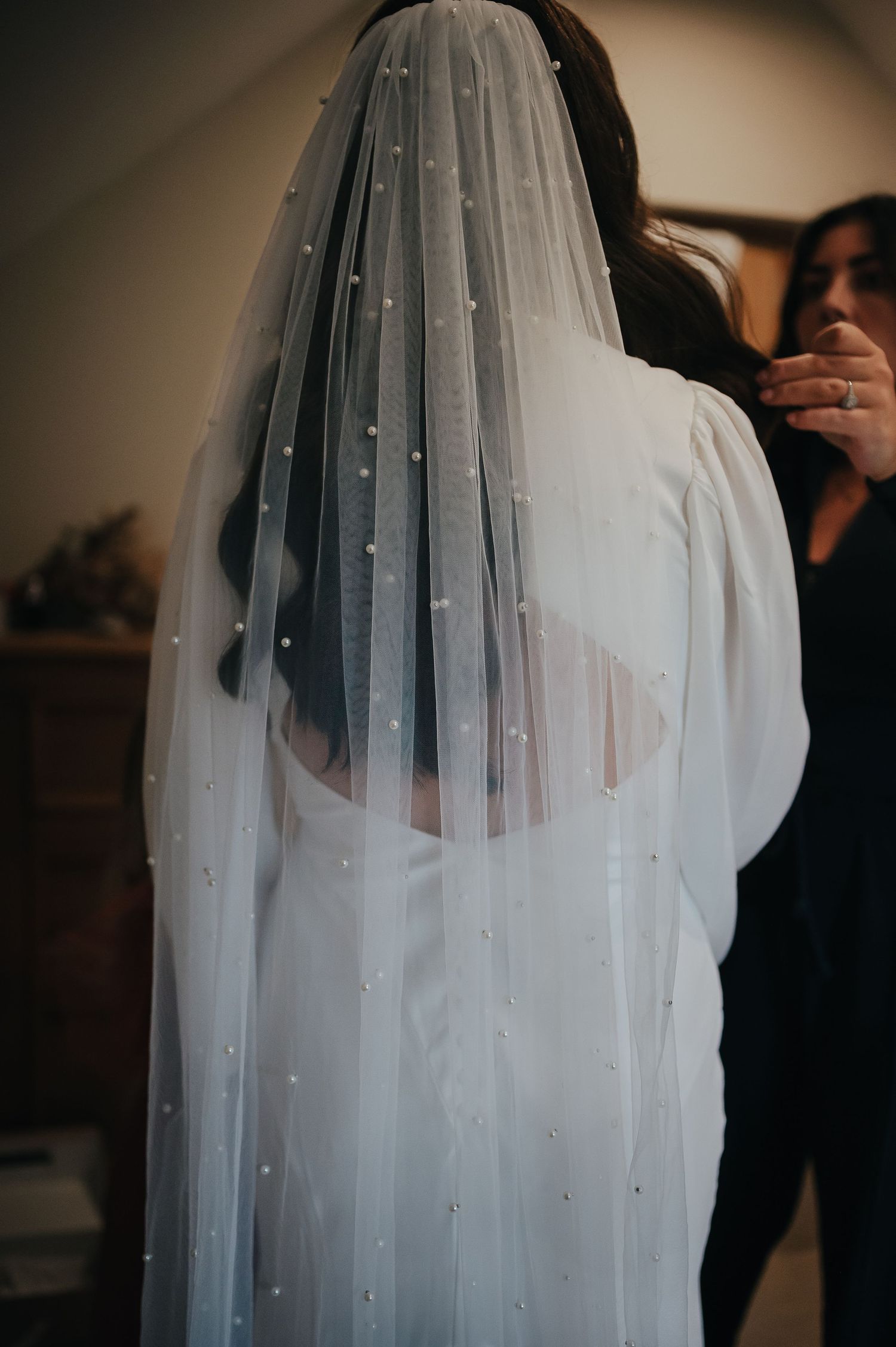 A pearl-studded wedding veil flows over a white dress in moody lighting.