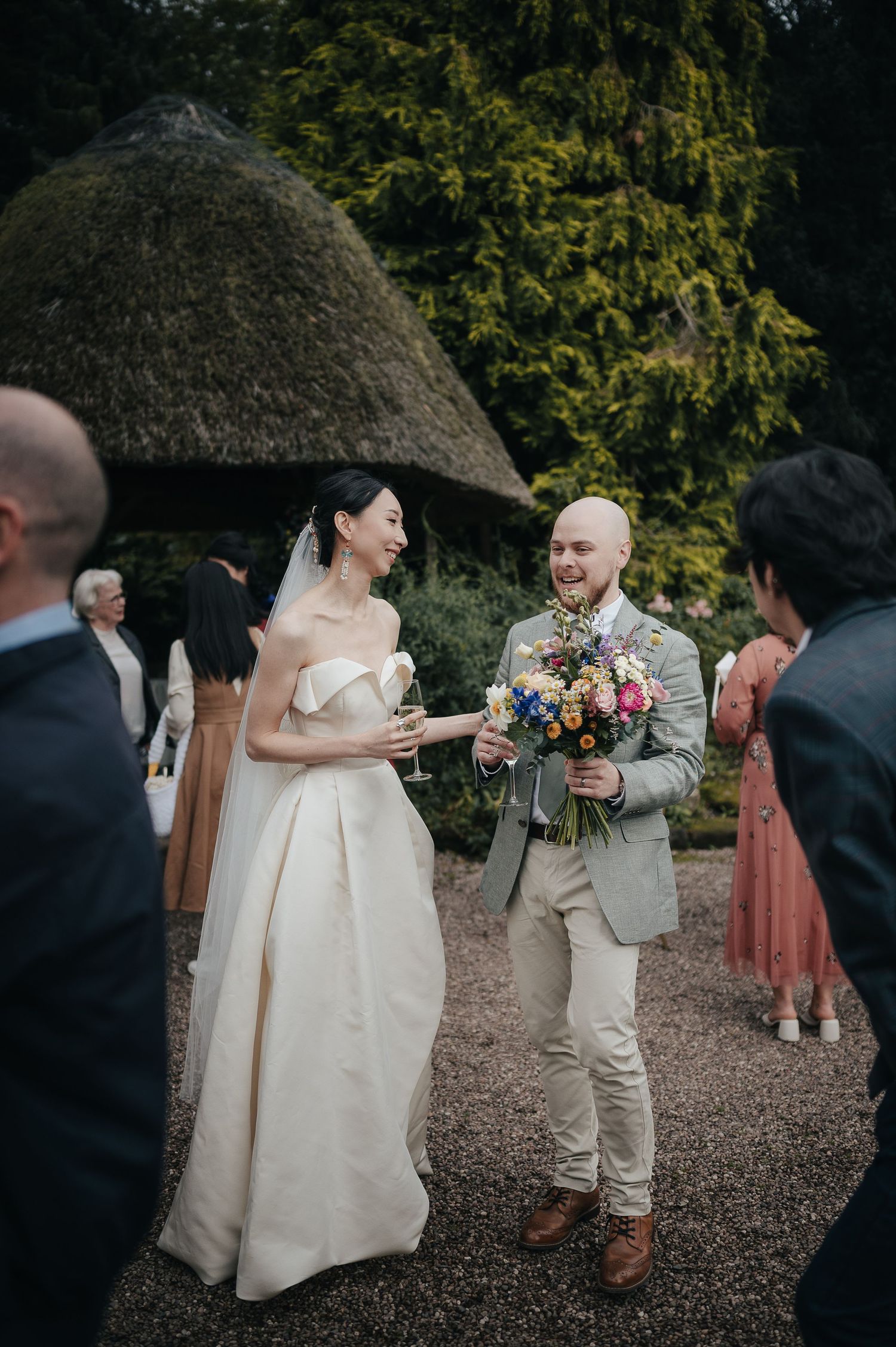 Wedding couple exchanges flowers during outdoor garden ceremony with guests looking on.