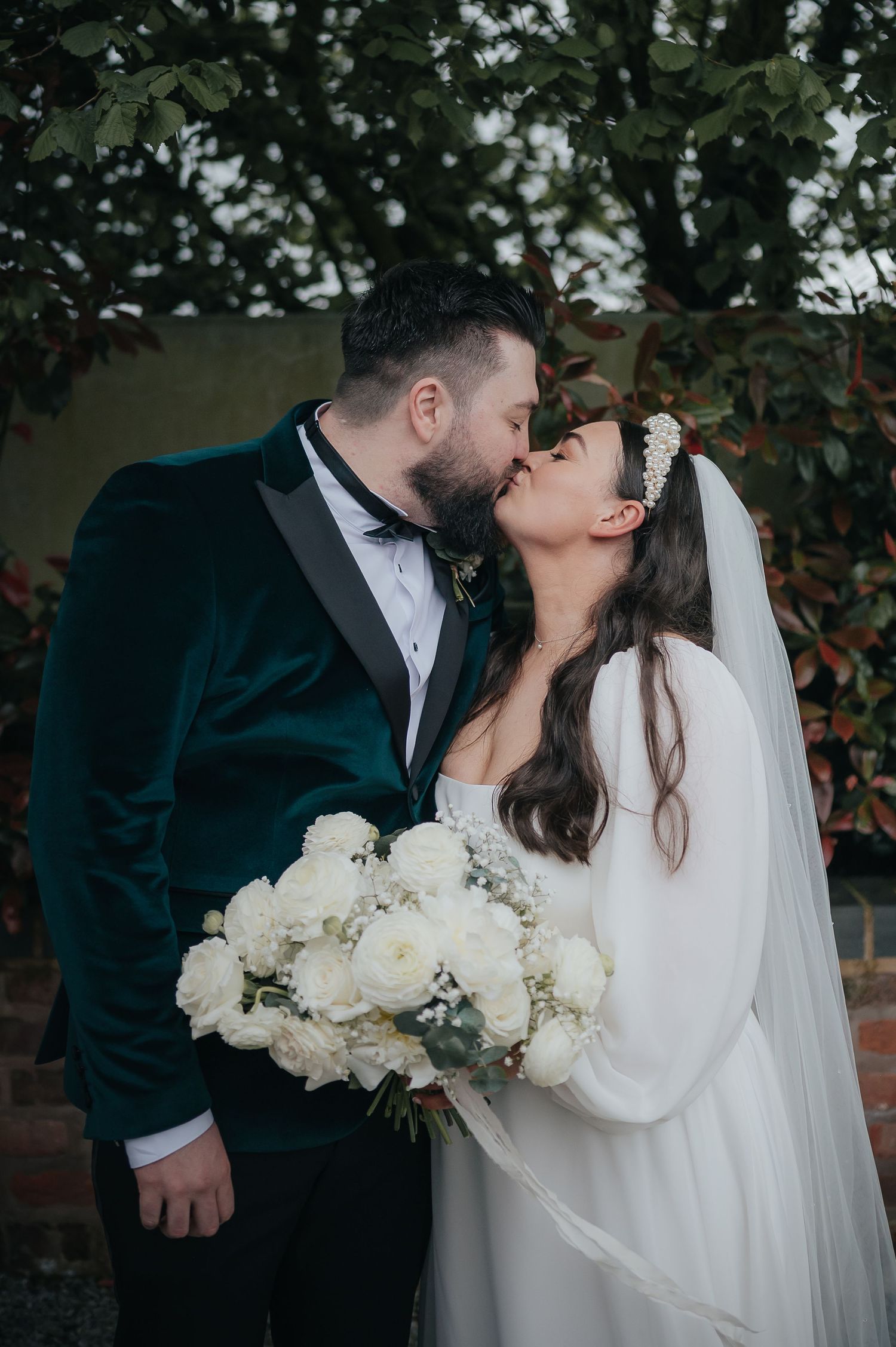 Romantic wedding portrait with white roses against brick wall backdrop.