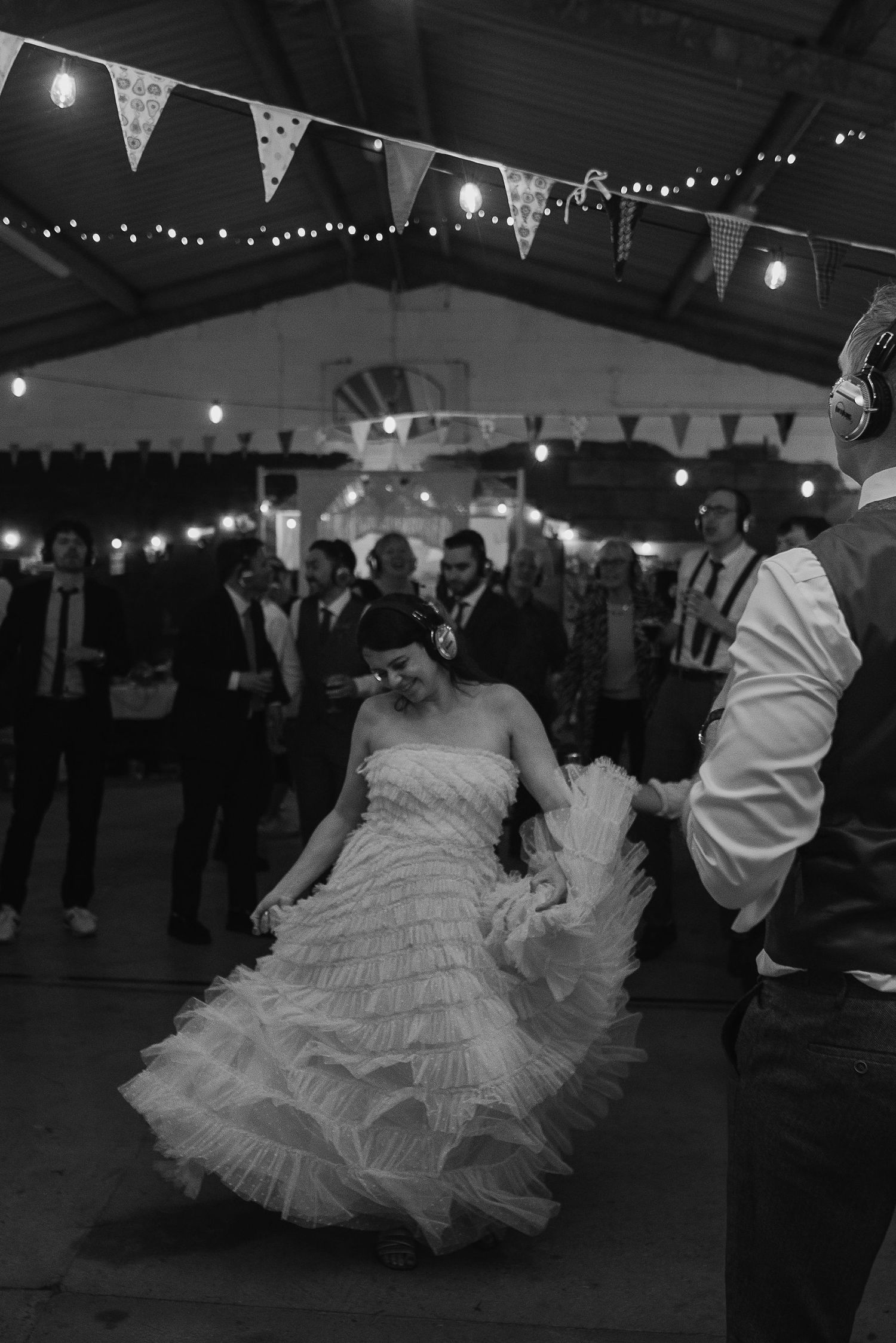 A bride twirls her layered wedding dress on the dance floor under string lights and bunting.