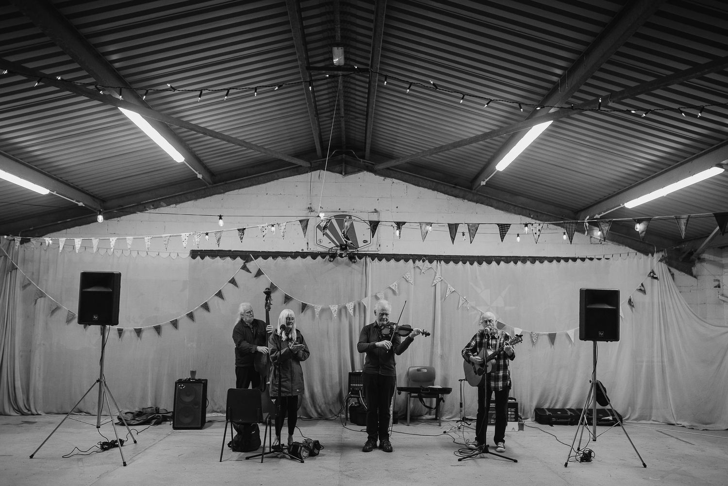 A band performs on stage with instruments under string lights and bunting in a white room.