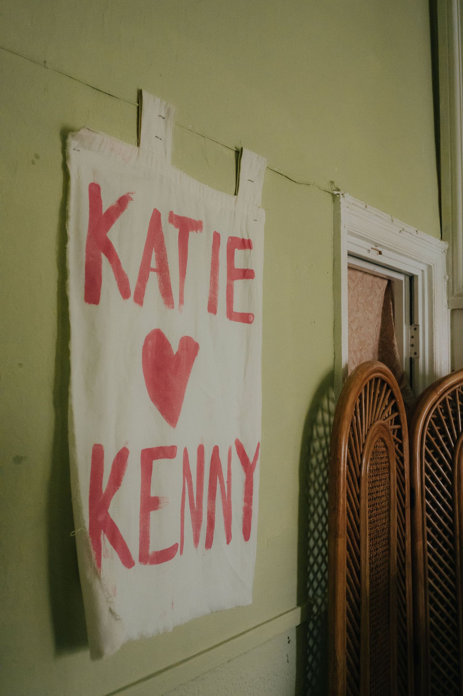 Handmade sign with 'Katie hearts Kenny' written in pink letters on white fabric.