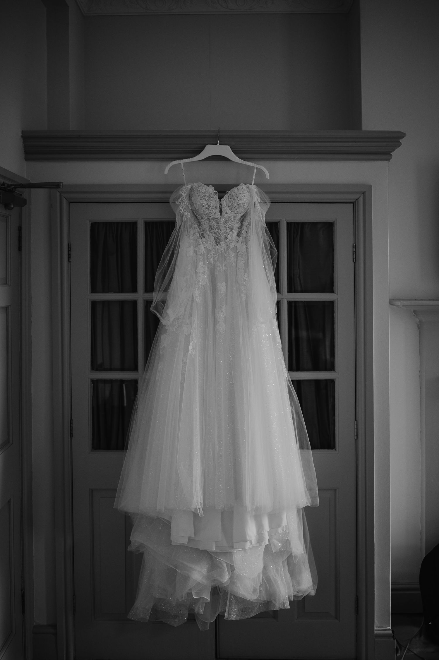 White lace wedding dress with sweetheart neckline hanging against a window frame.