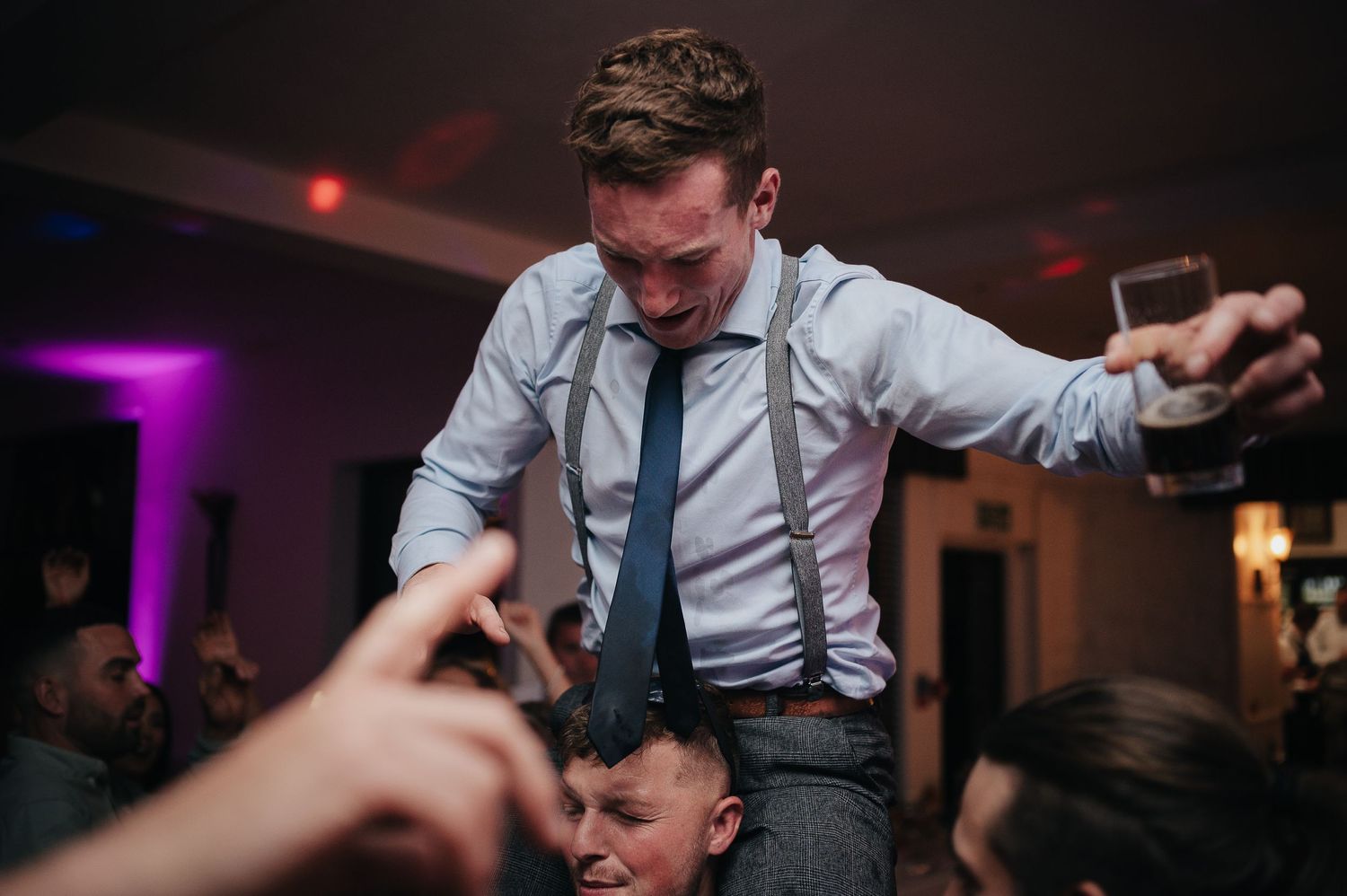 Energetic wedding reception dancing with guests lifting someone on the dance floor.