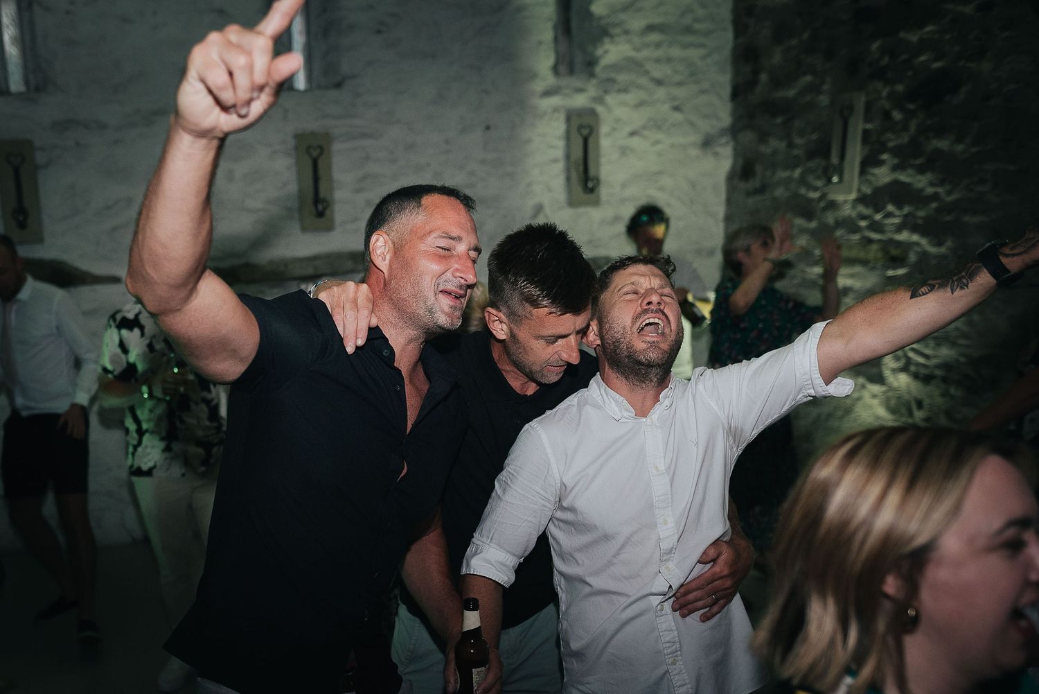 Wedding guests dancing enthusiastically at a lively reception party with arms raised.