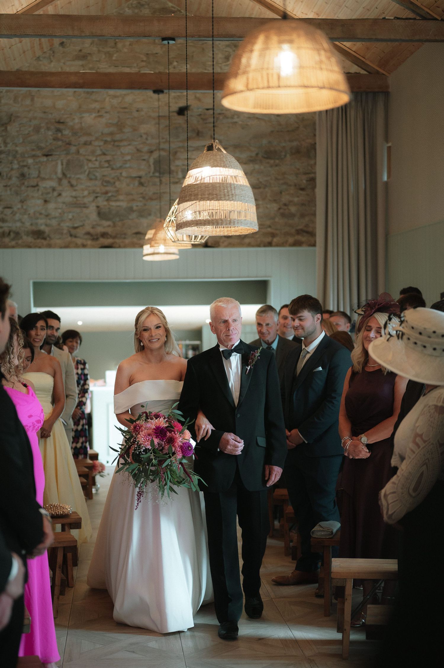 Wedding reception in a rustic venue with stone walls and pendant lighting as guests mingle during the celebration.