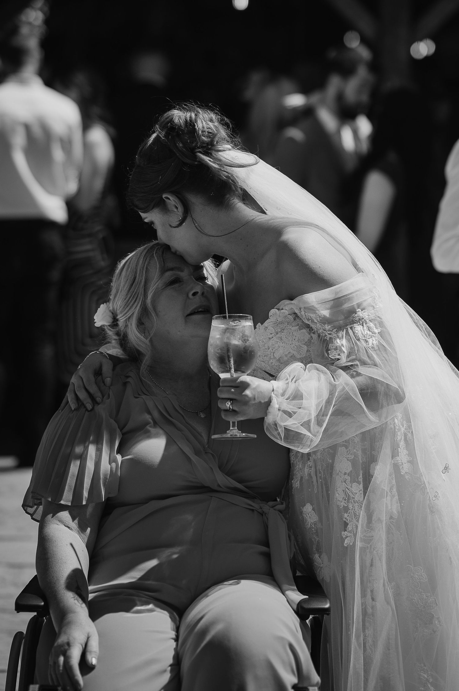 A tender moment captured between a bride in white dress and wedding guest sharing a drink.