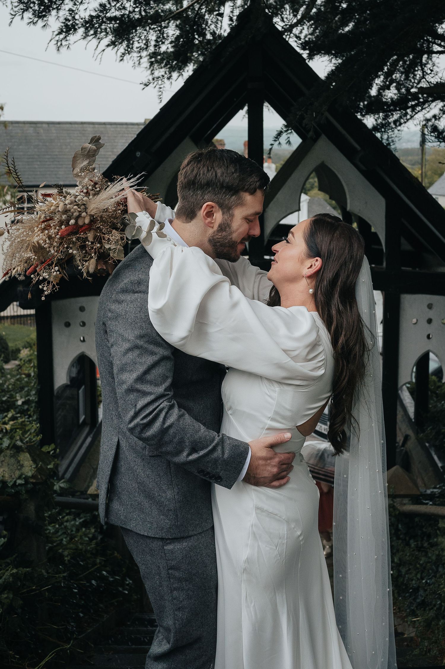 A couple embraces under a rustic wooden arch during their wedding ceremony.