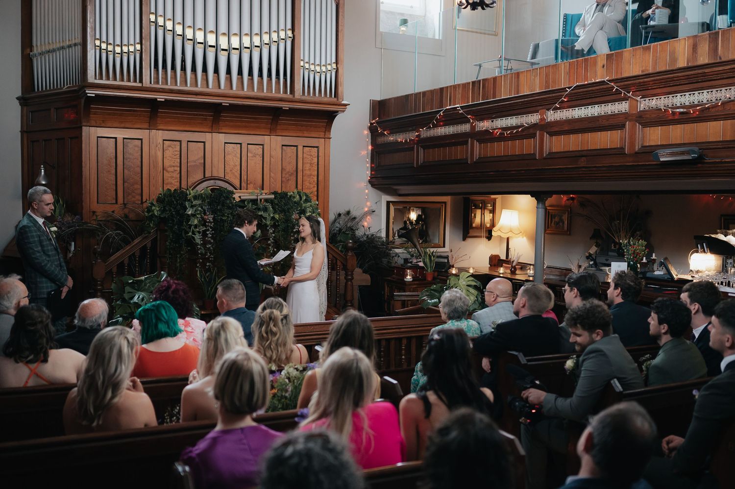 A wedding ceremony in progress inside a traditional church with wooden pews and organ pipes.
