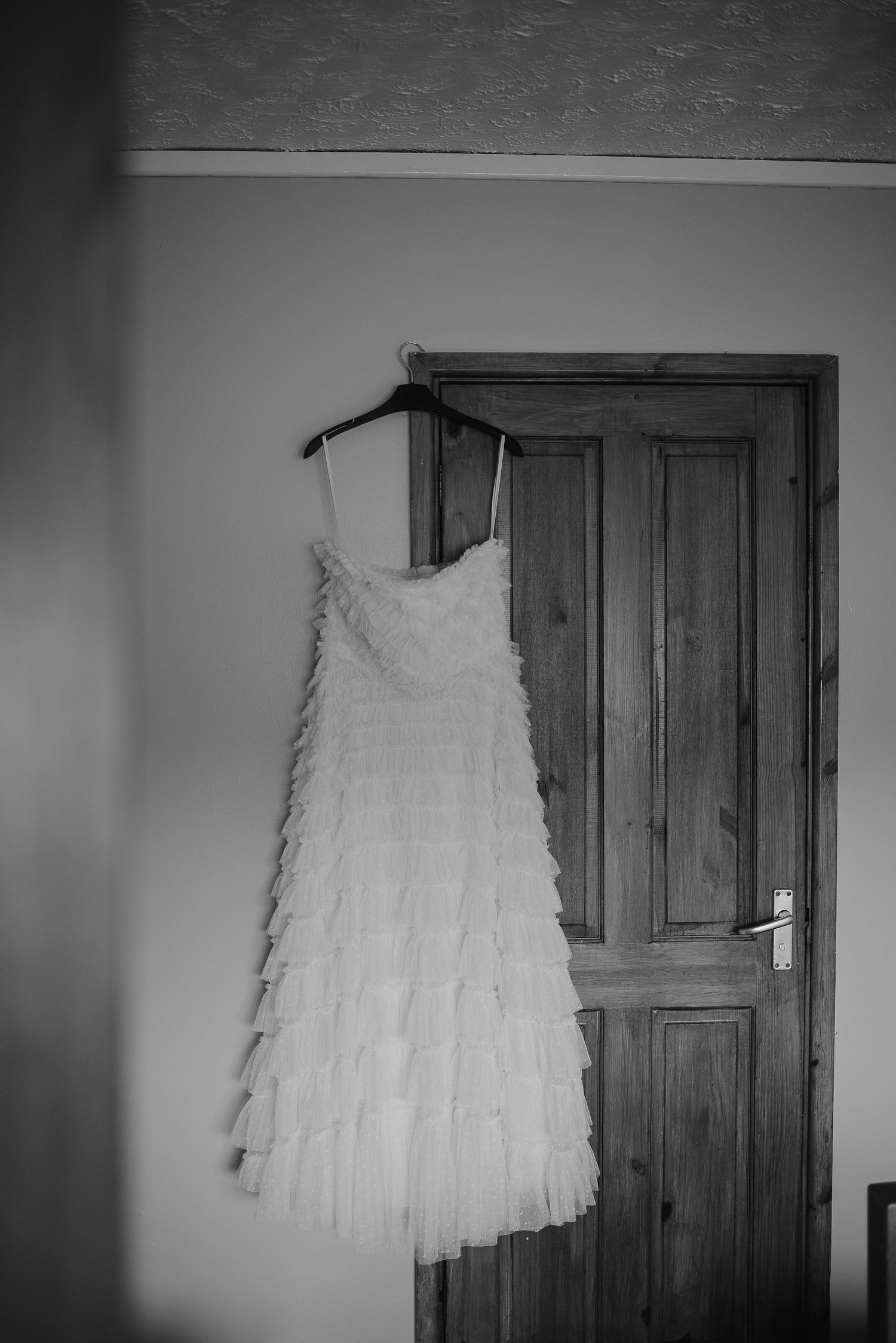 White layered wedding dress hanging on wooden door in black and white photography.