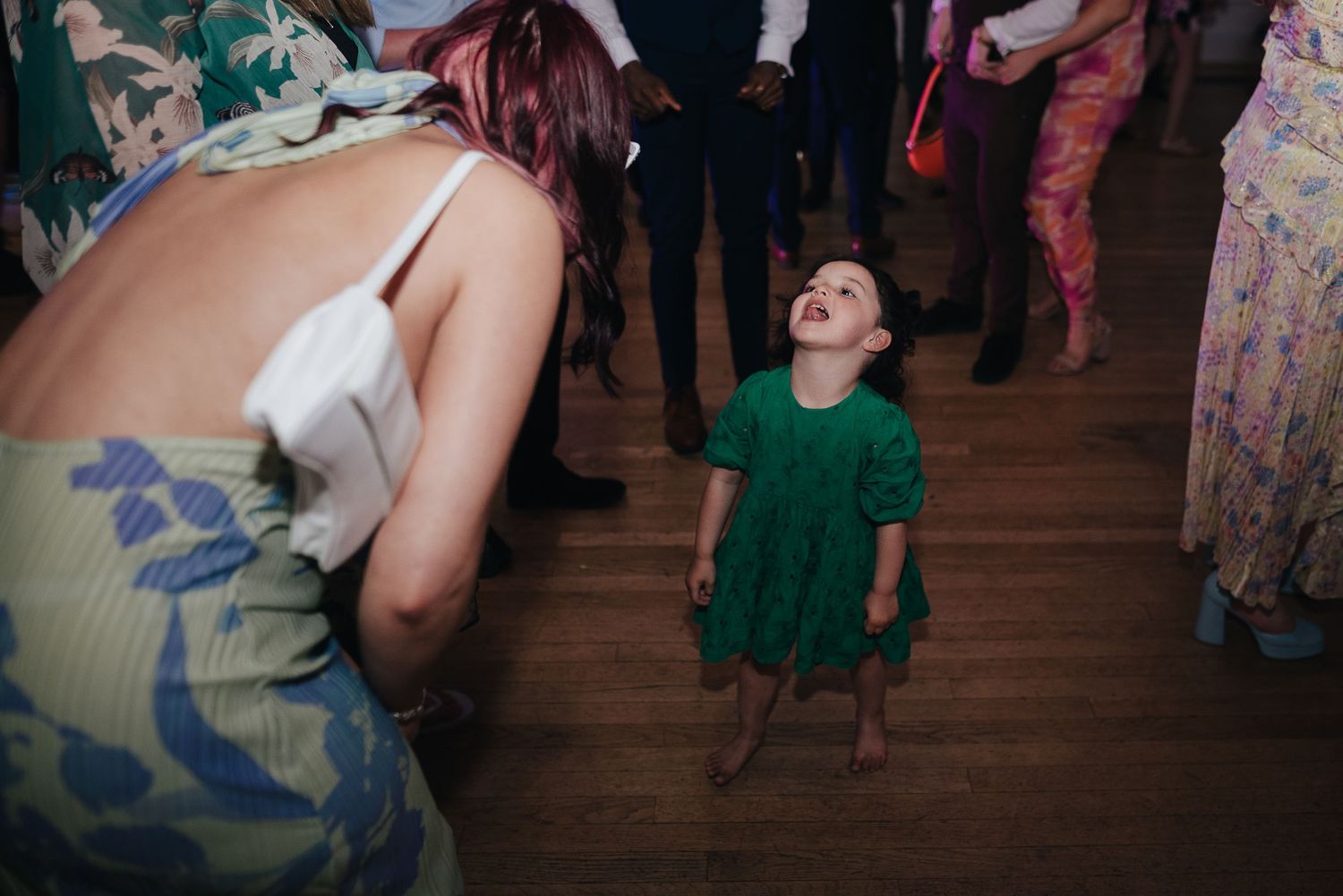 A young guest in a green dress dancing on a wooden floor.