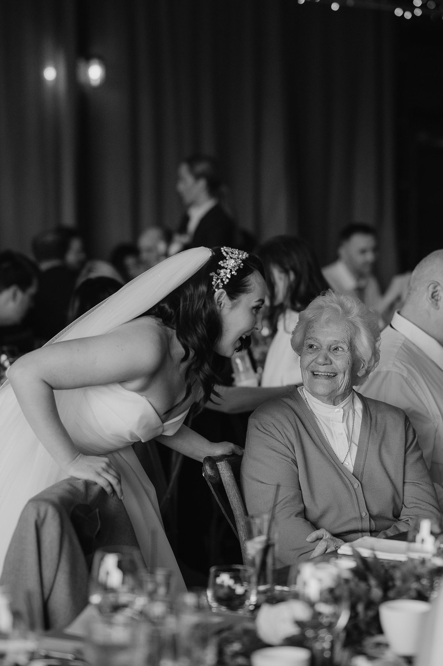 A candid black and white moment during a wedding reception with string lights in the background.