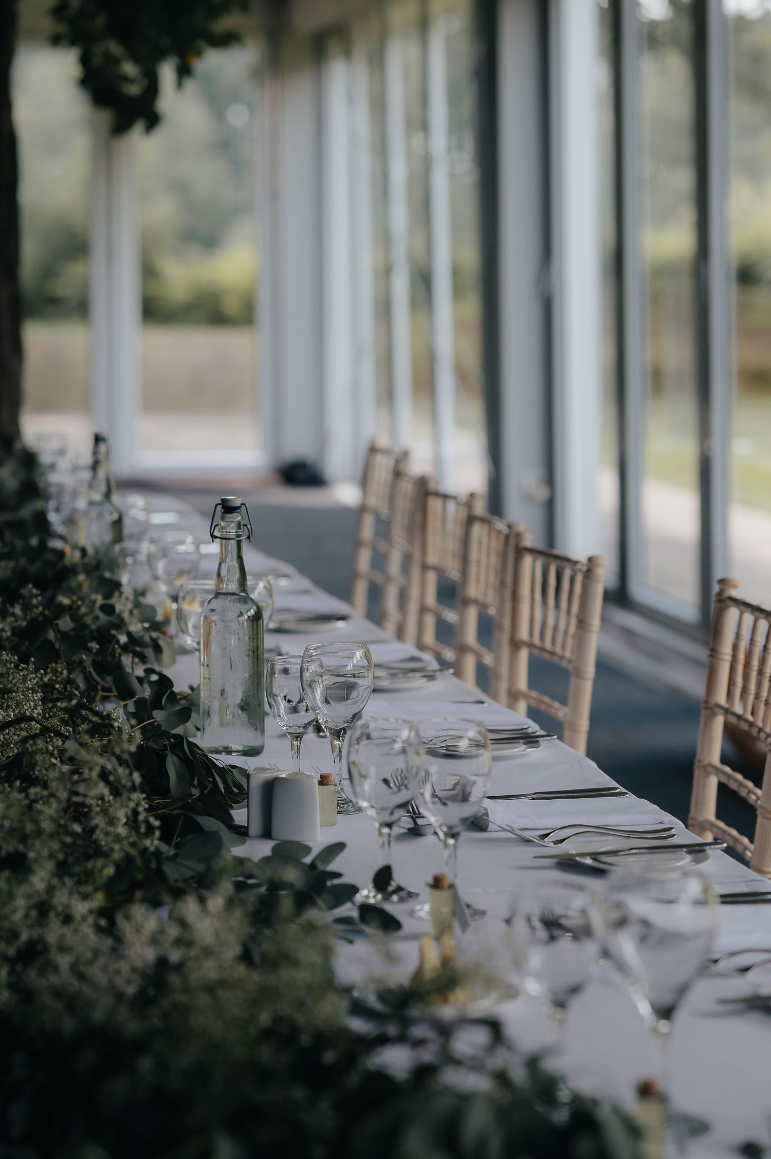 Elegant wedding reception table setting with white linens and natural greenery decor.