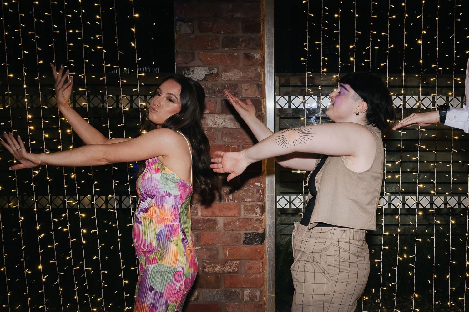 Two wedding guests strike dramatic poses against a backdrop of twinkle lights.