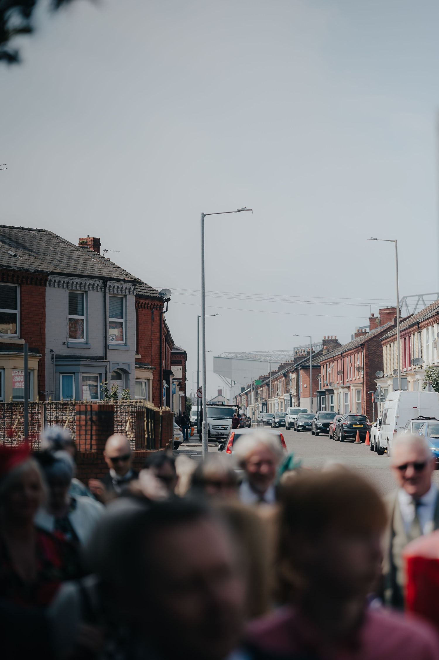 A crowd of wedding guests gathered on a residential street with traditional brick houses.