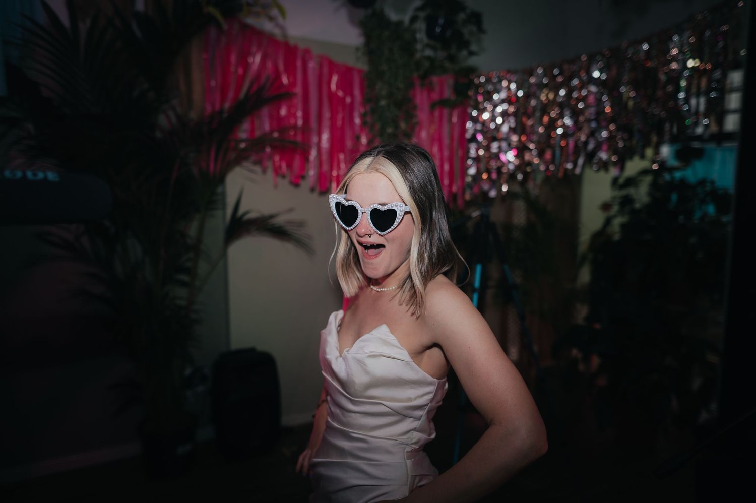 Bride in white dress and sunglasses dancing at wedding reception with pink decorations.