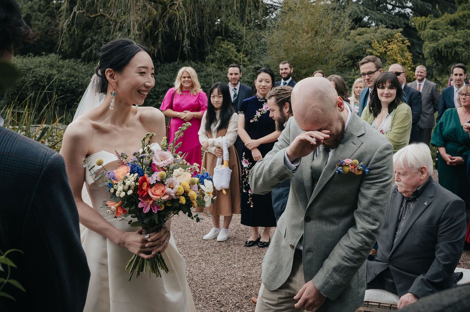 Emotional wedding ceremony moment outdoors with guests watching and a colorful bouquet.