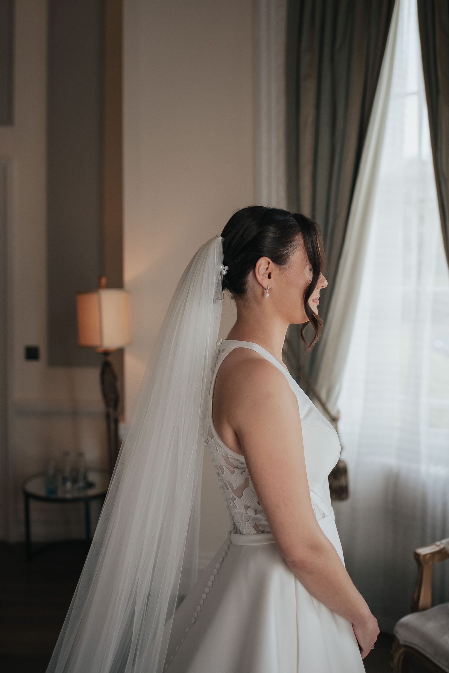 Classic white wedding dress and flowing veil captured in soft window light.