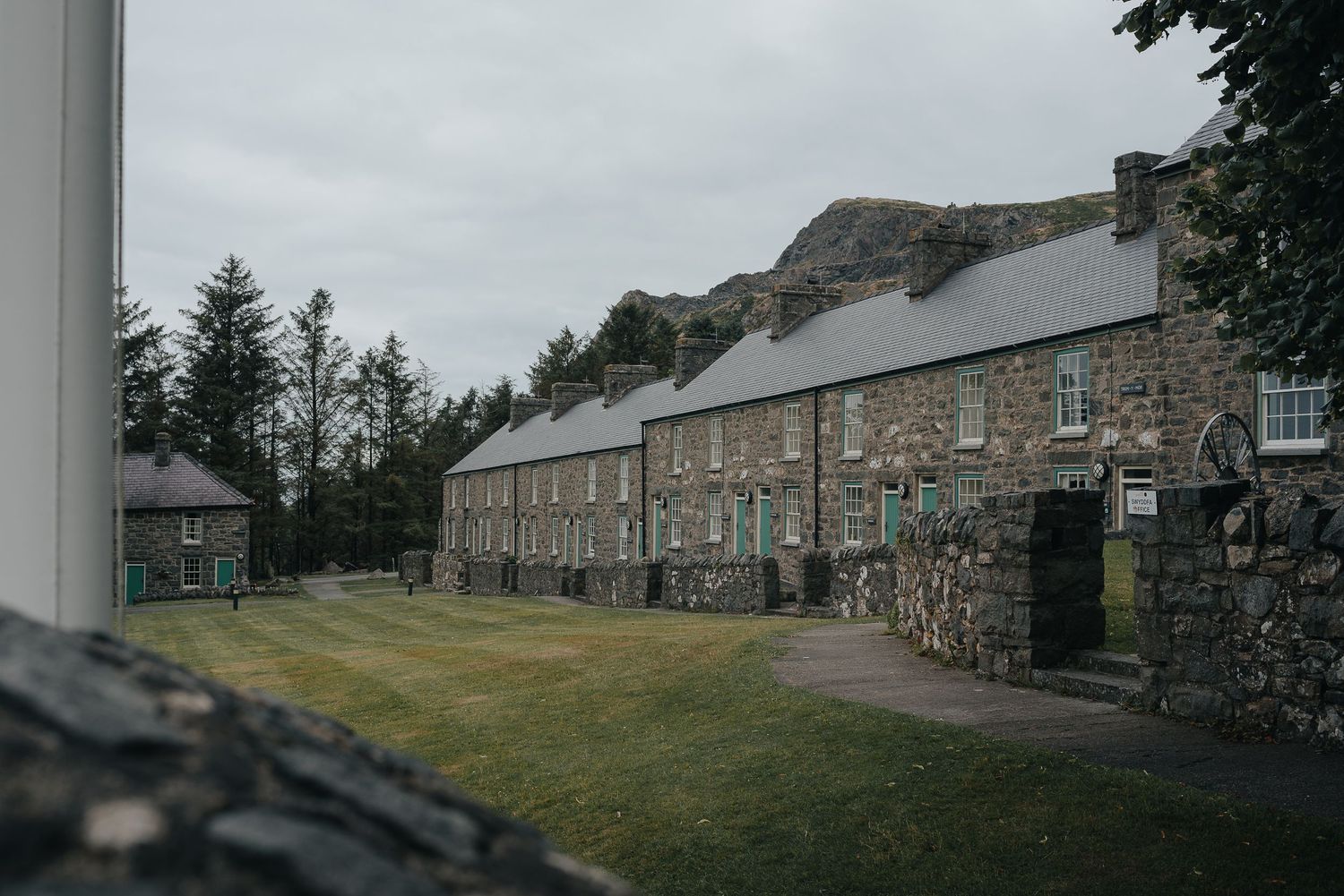 Row of traditional stone cottages with gray slate roofs along a grassy path.