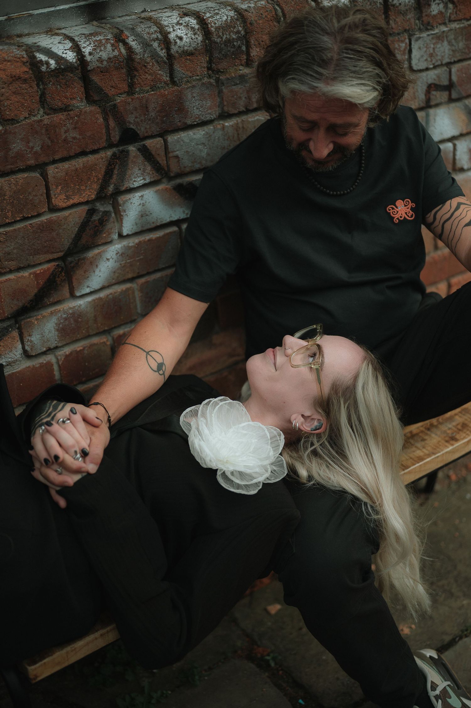 A series of photos showing two people in black clothing reclining on a wooden bench against a brick wall.
