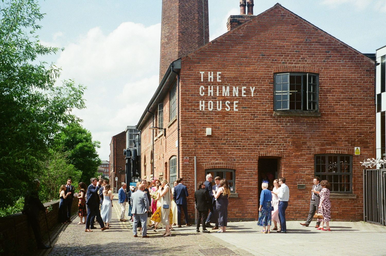 Guests gather outside The Chimney House, a historic red brick venue, on a sunny day for a special event.