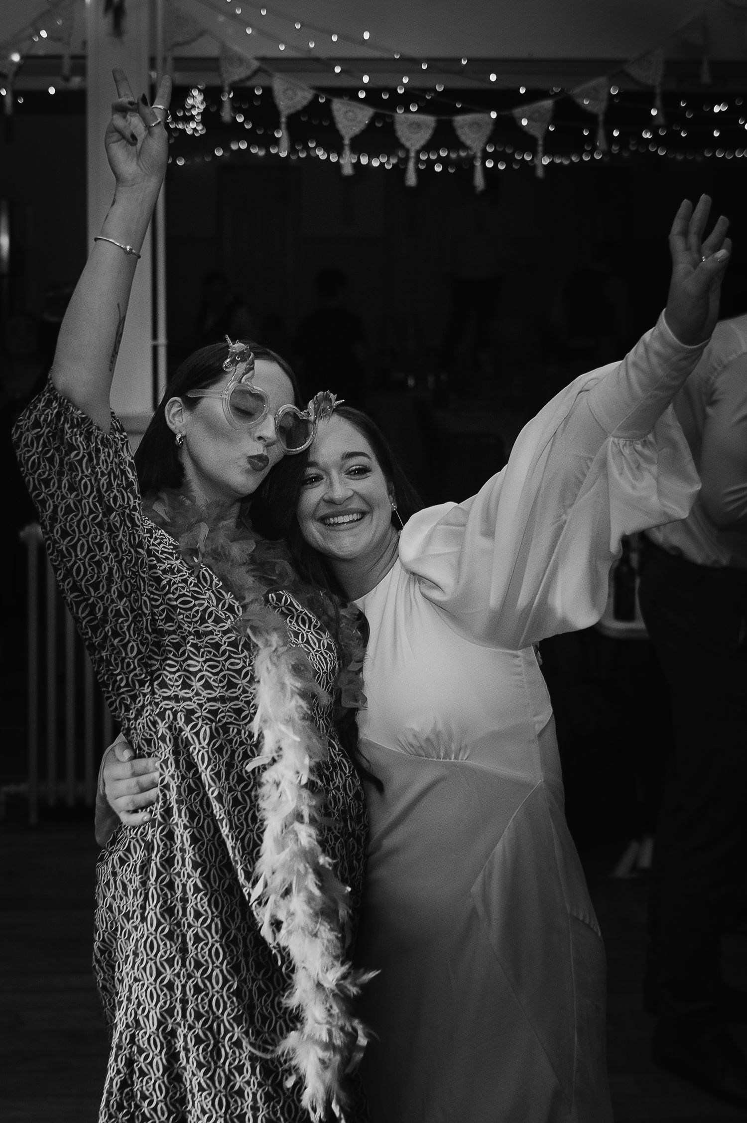 Black and white photo of wedding celebration with guests dancing under string lights.