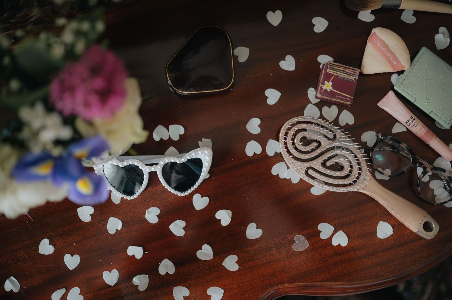 Heart-shaped sunglasses and decorative items arranged on wooden surface with scattered paper hearts.