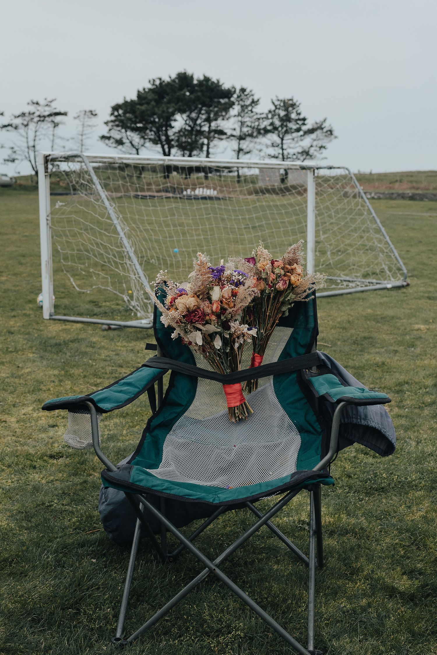 Wedding bouquet rests on camping chair with soccer goal in background.