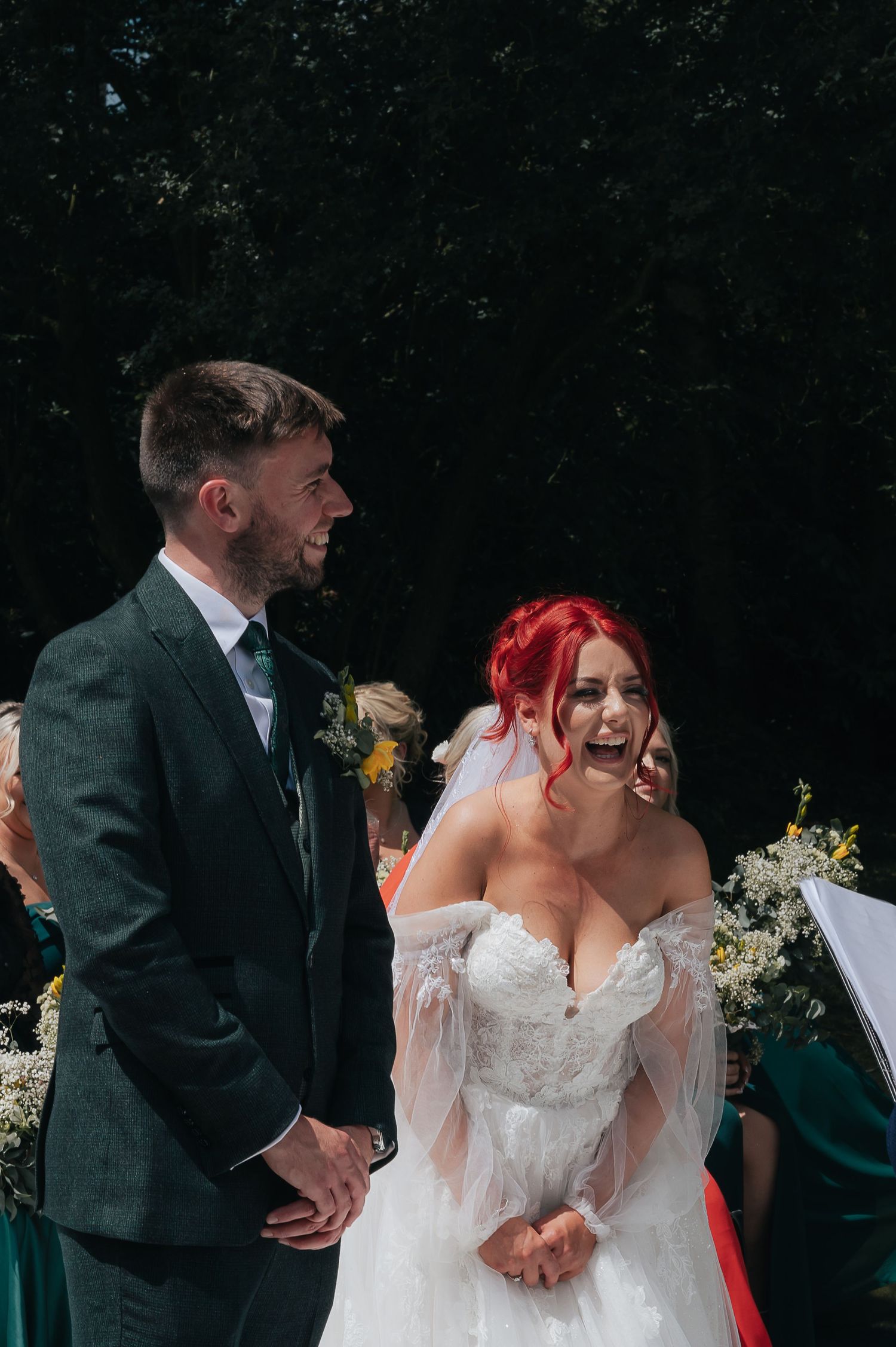 A wedding ceremony outdoors with a couple standing together against a dark background.