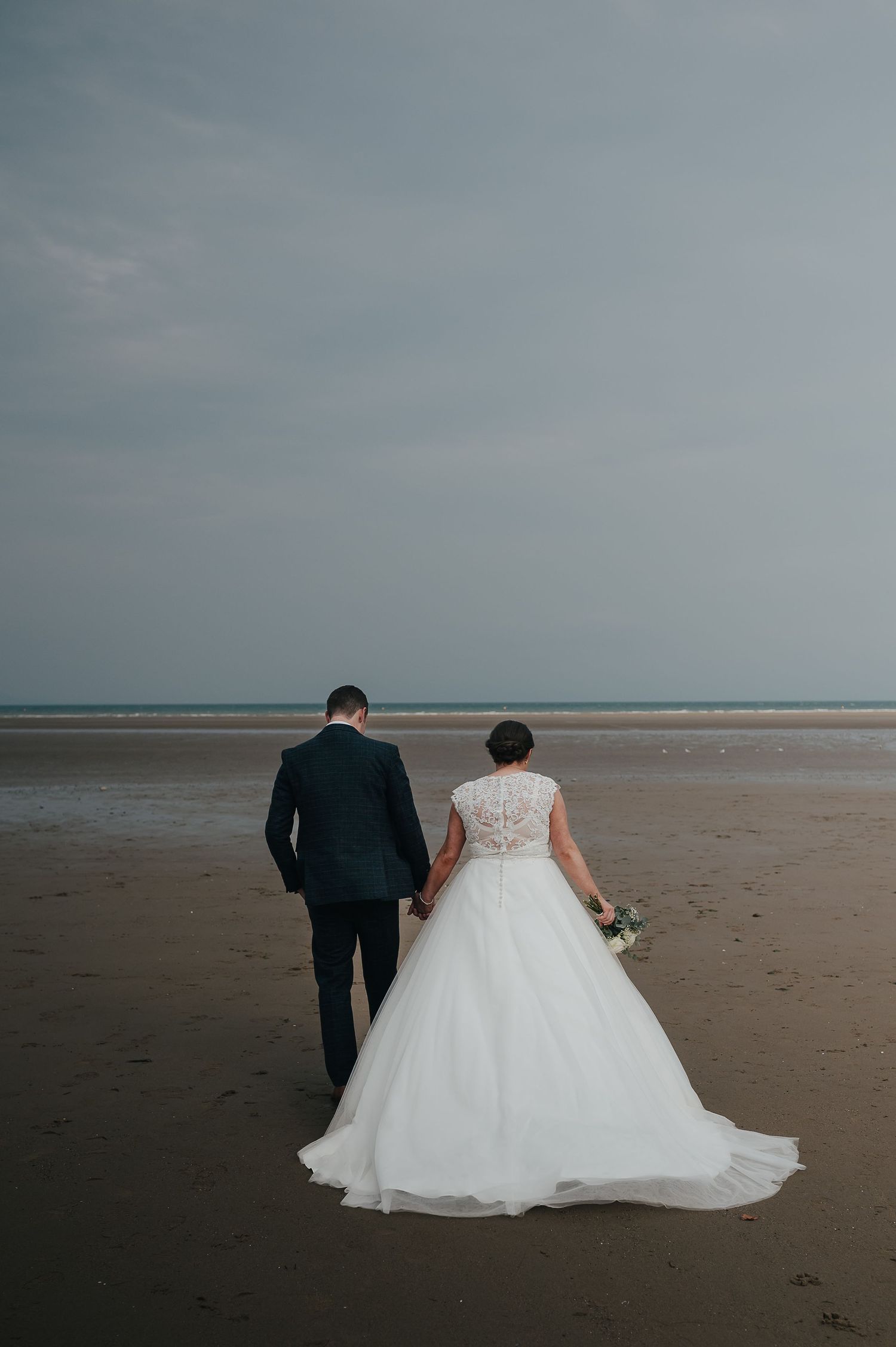 A couple walks hand in hand on a serene beach during their wedding day.