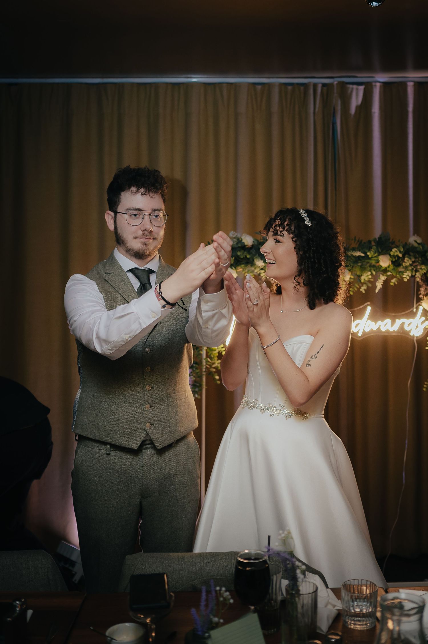 Newlyweds share a celebratory moment during their wedding reception under glowing decor.