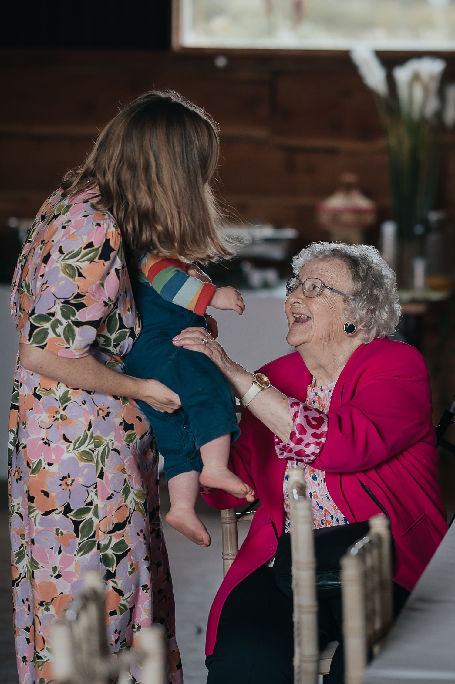 Heartwarming moment between guests and elderly woman in bright pink cardigan at wedding reception.