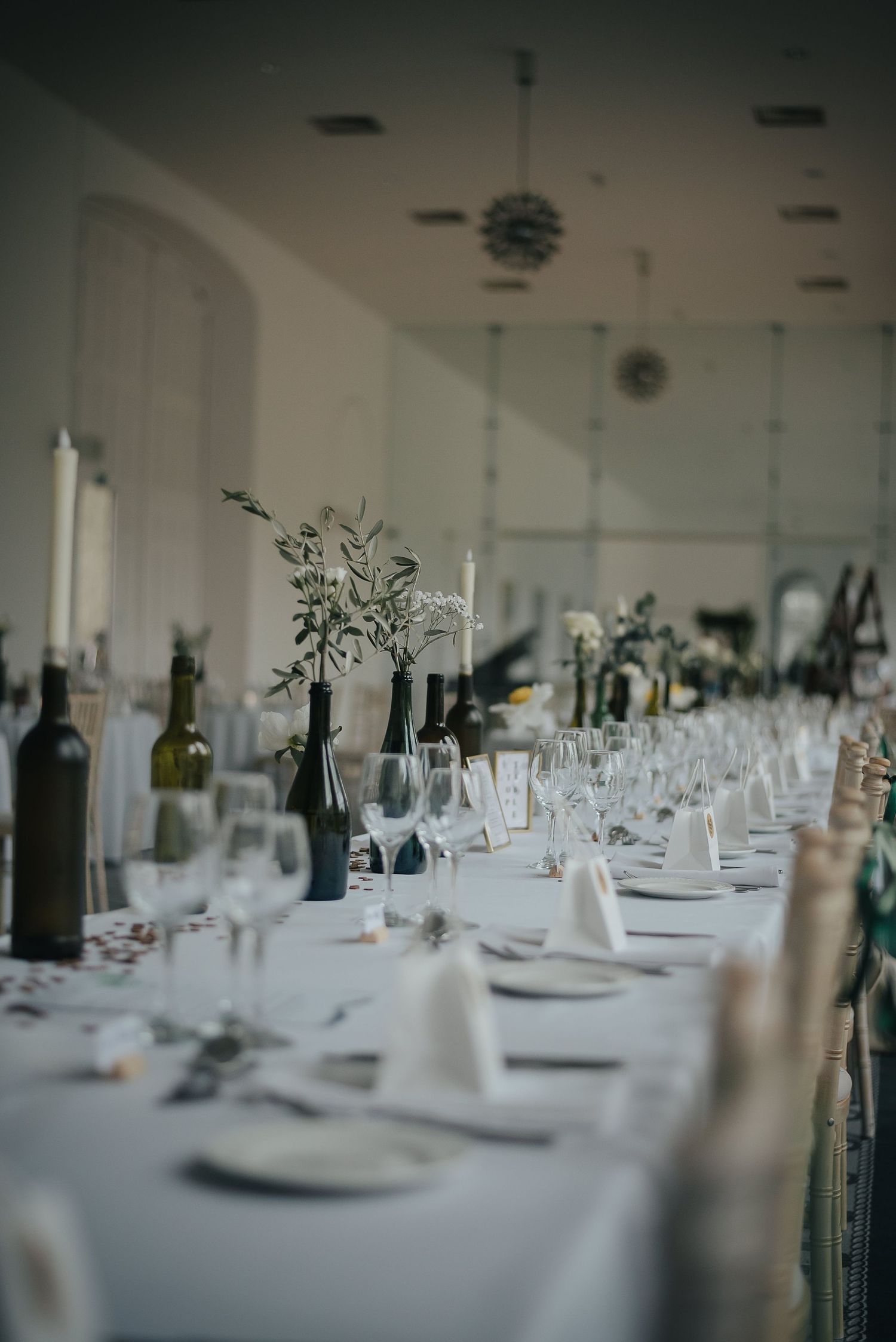 Elegant wedding reception table setting with wine bottles, white linens and floral centerpieces.