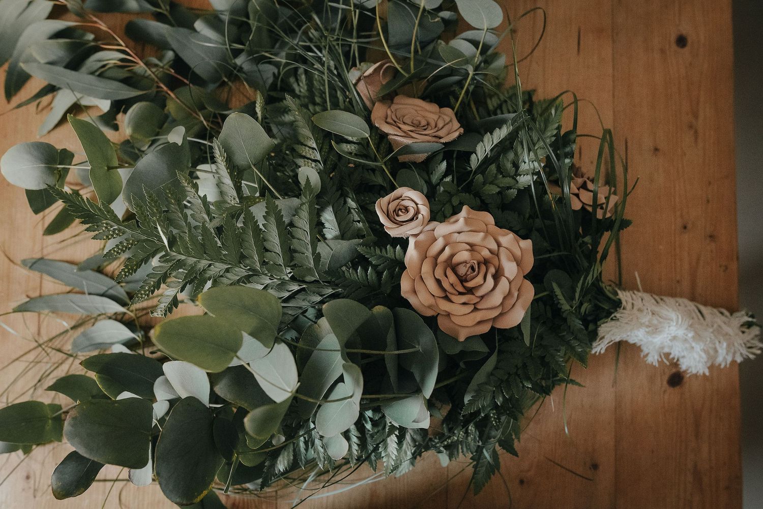 Elegant wedding bouquet with peach roses and eucalyptus on wooden surface.
