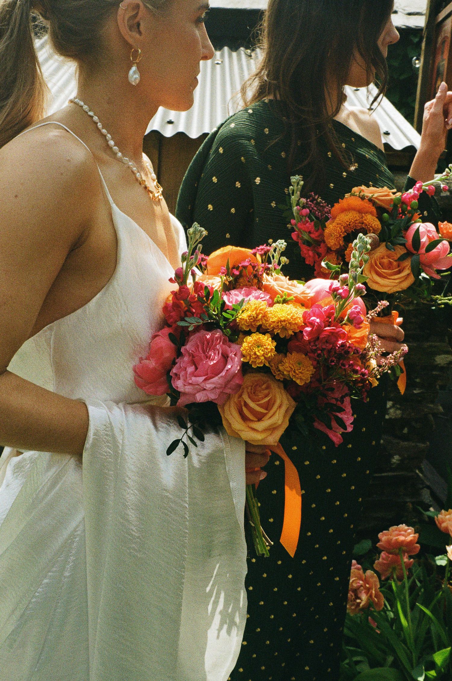 Bride in white dress holding vibrant pink, orange, and yellow wedding bouquet tied with orange ribbon.