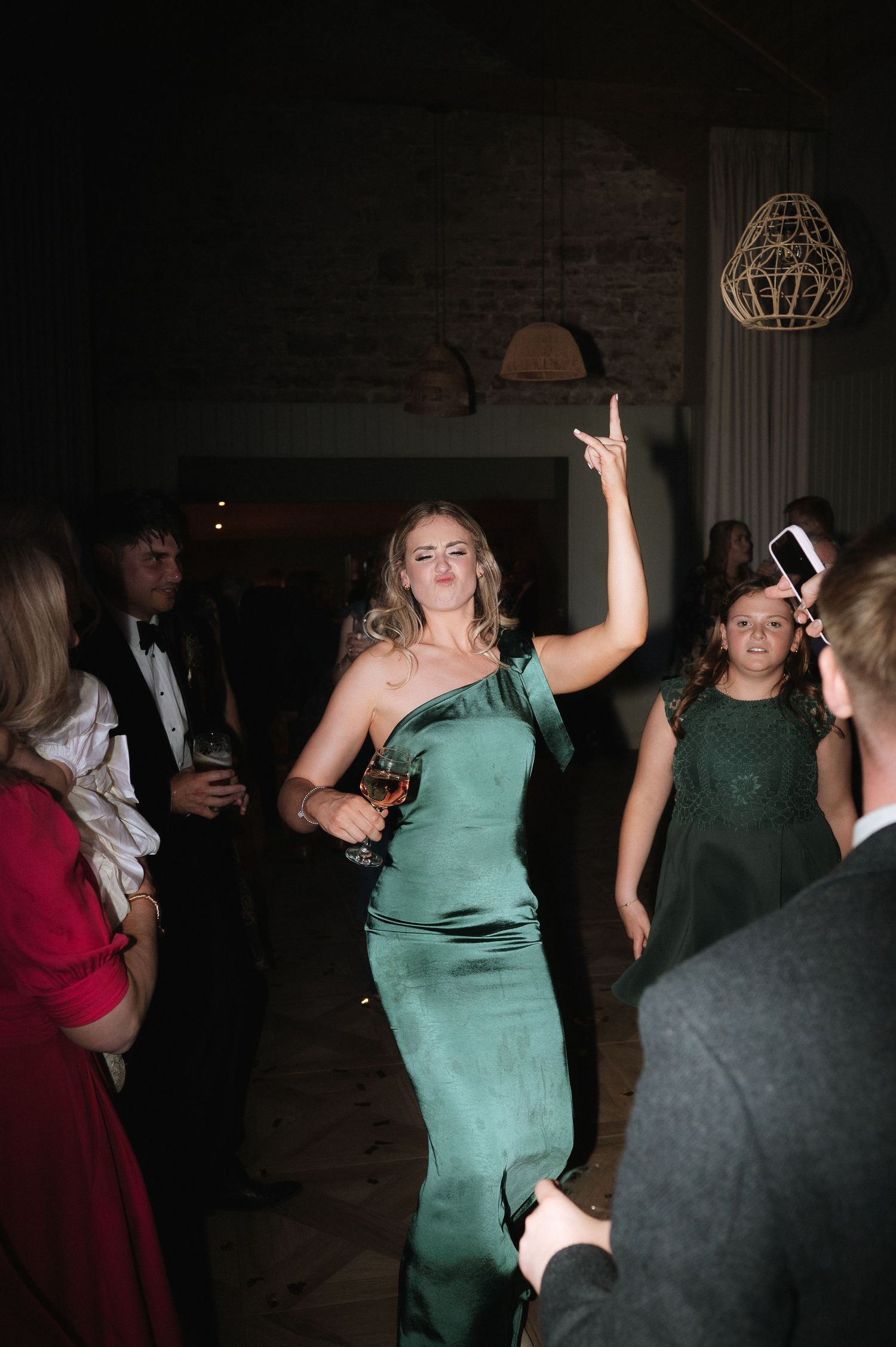 Wedding reception dance party with guests in formal attire under dim lighting.