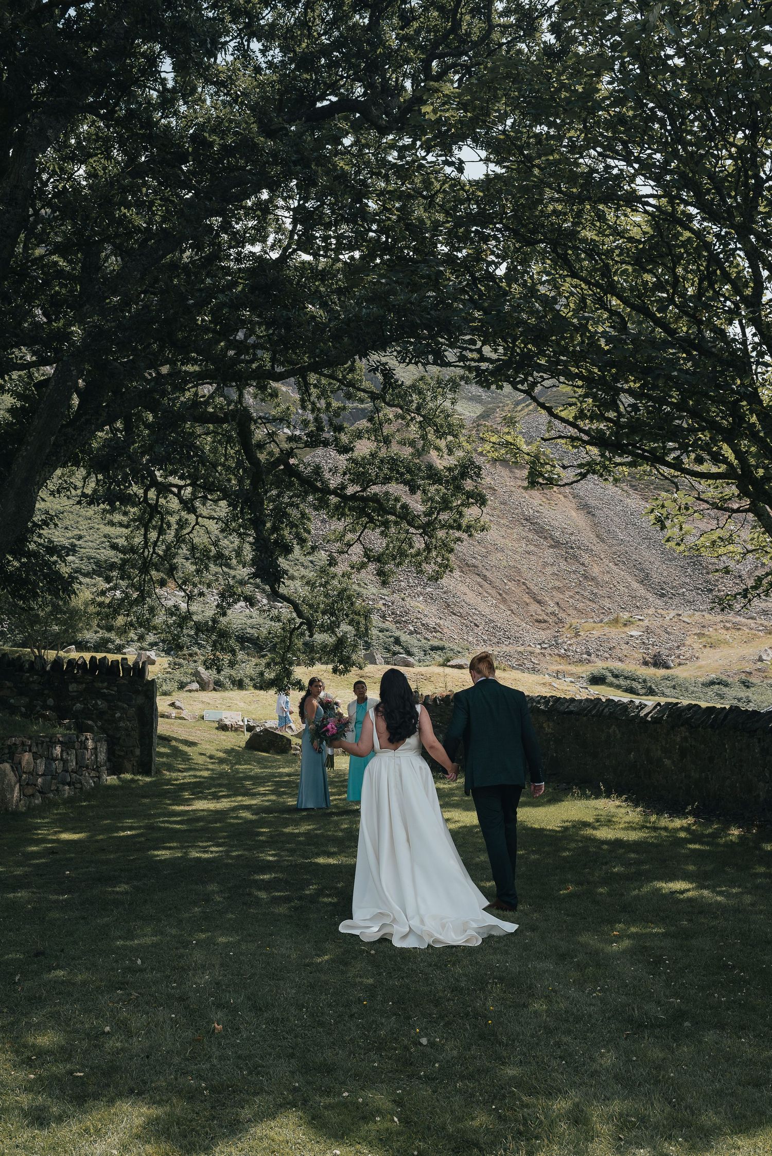 Wedding guests walking through a garden path with mountains in the background.