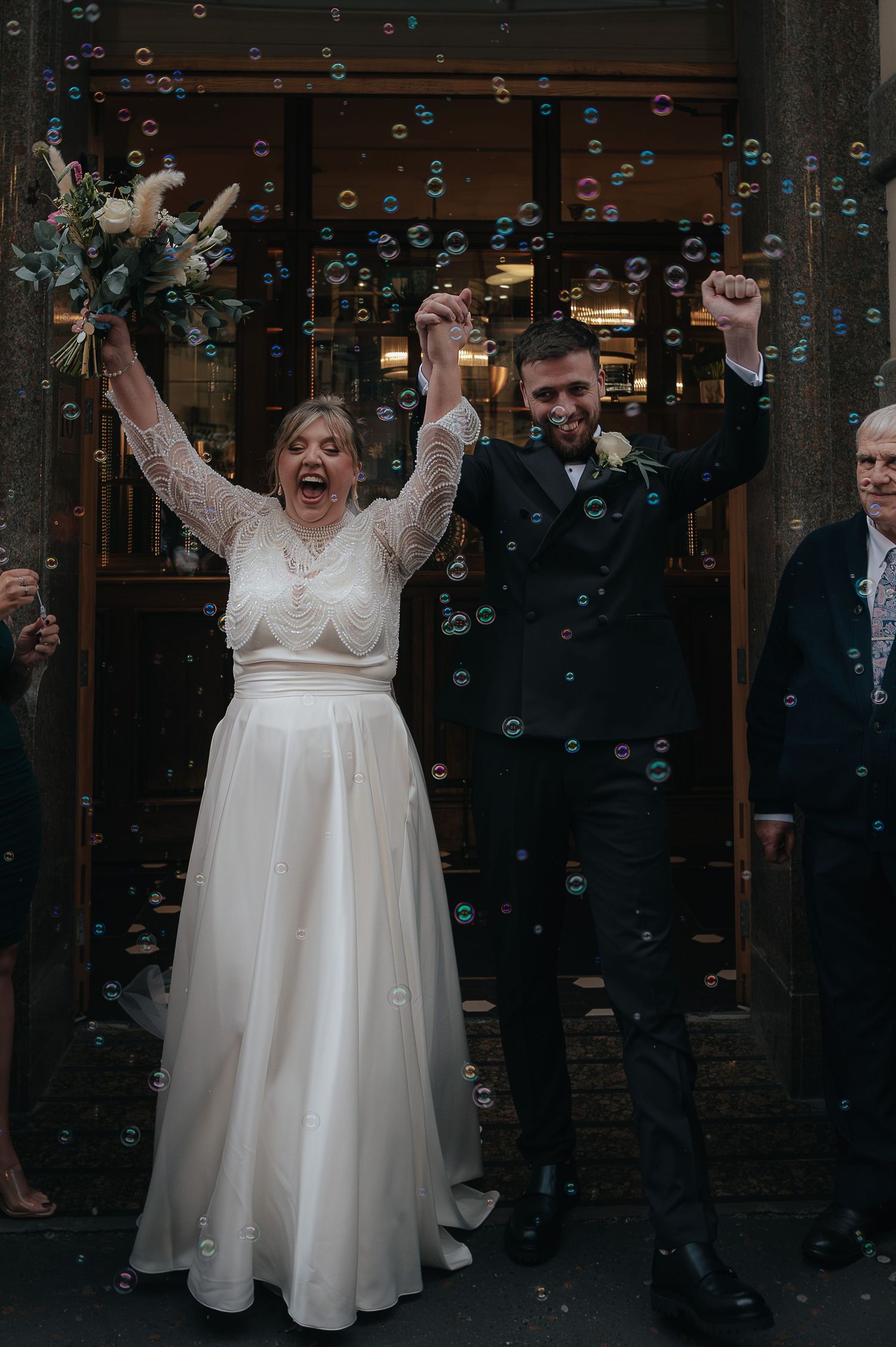 A person in a white wedding dress twirls joyfully while celebratory bubbles float through the dark evening air.