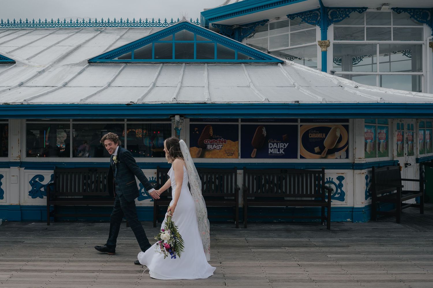 Wedding couple walking along a blue and white seaside pier.
