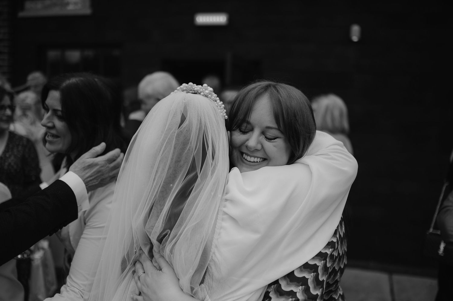 Black and white photo of wedding guests sharing emotional embraces during reception.