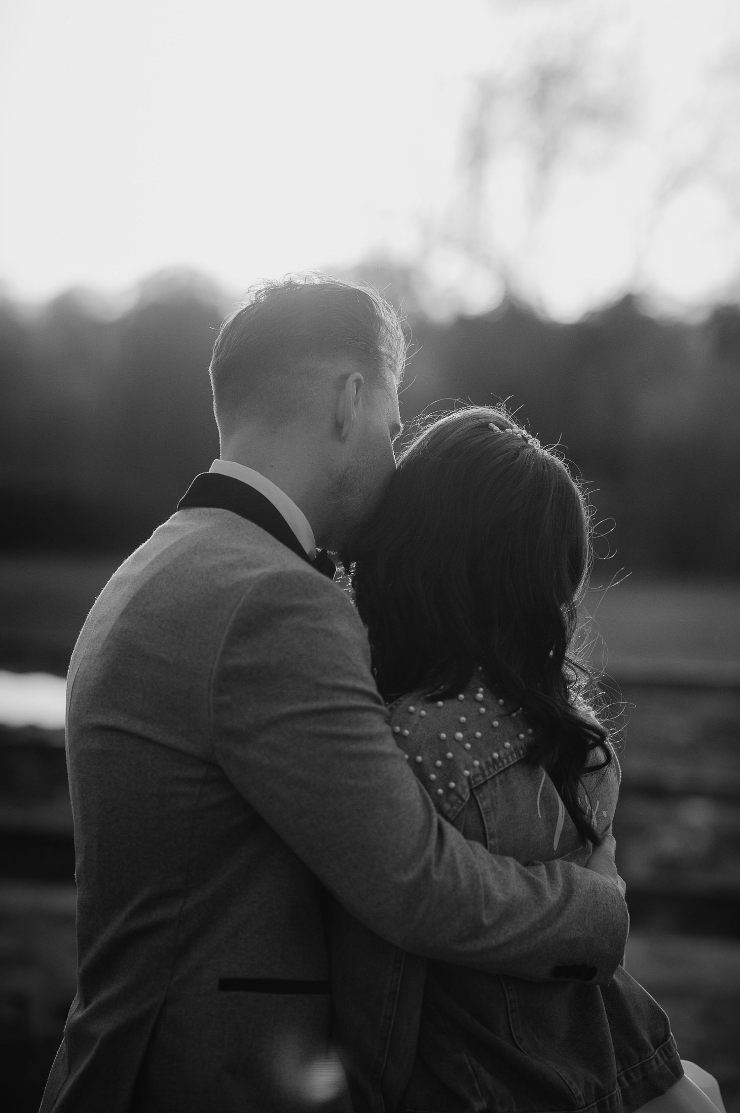 A black and white intimate portrait of a couple embracing at sunset.