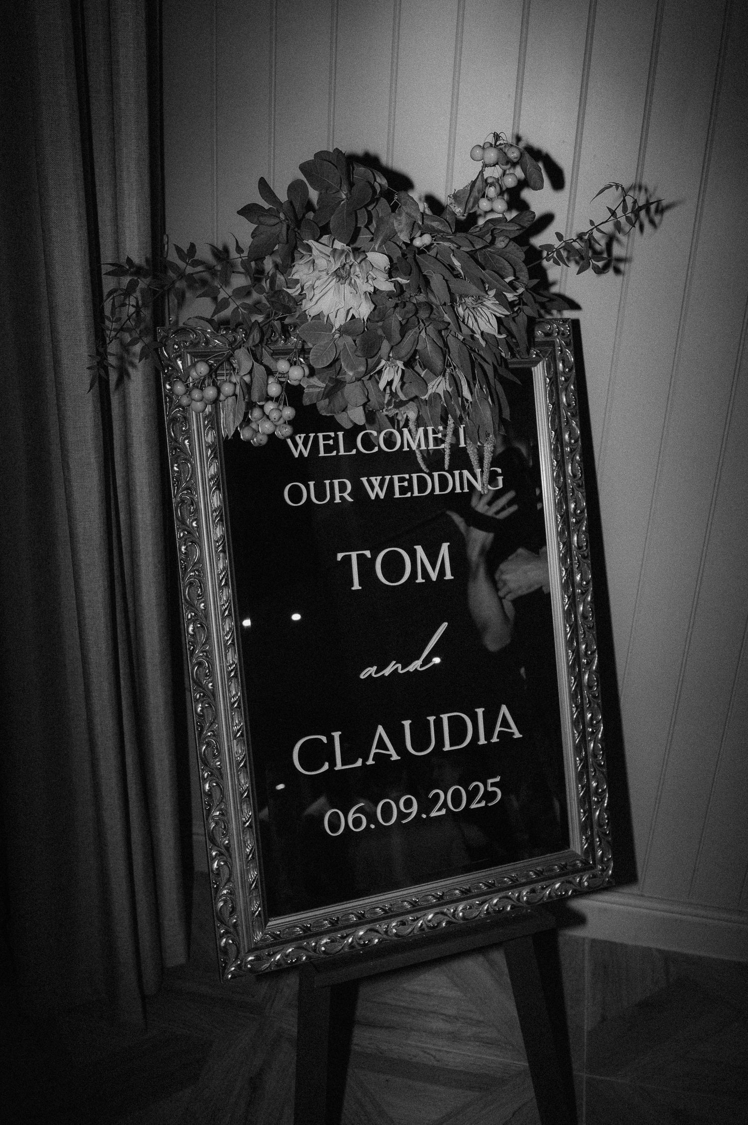 Black and white wedding welcome signs in ornate frames display the date and couple's names against a dark background.